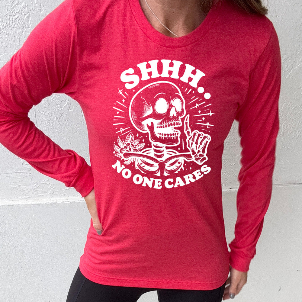 heather red long sleeve with the words "Shhh.. no one cares" on it, with the graphic of a skeleton holding a finger to its lips