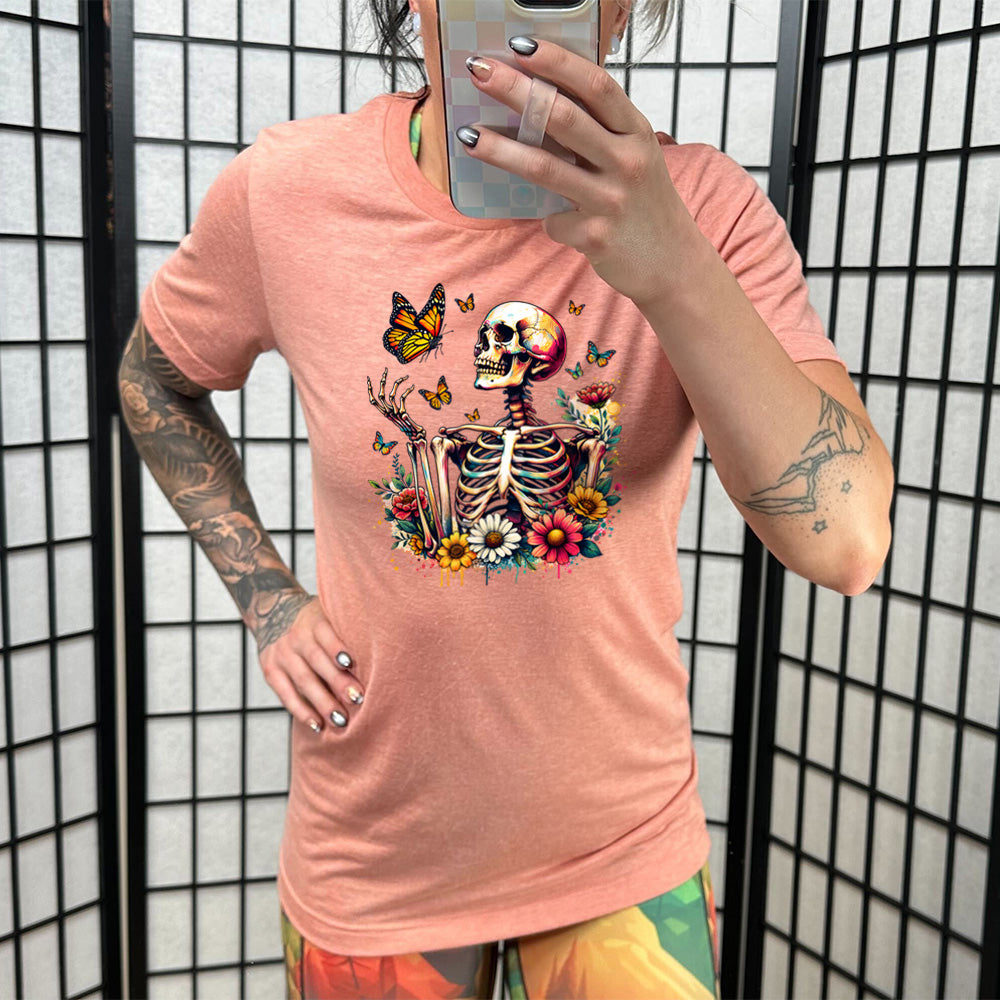 Sunset colored shirt with a skeleton, butterflies, and flowers graphic on it