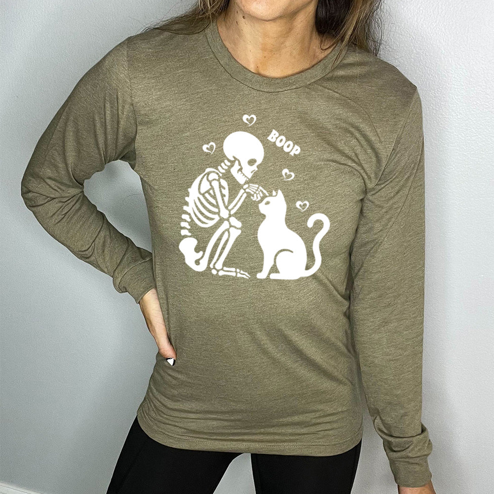 heather olive long sleeve shirt with the graphic of a sitting skeleton touching the head of a sitting cat, with the word "boop" above this action, and four little hearts around them
