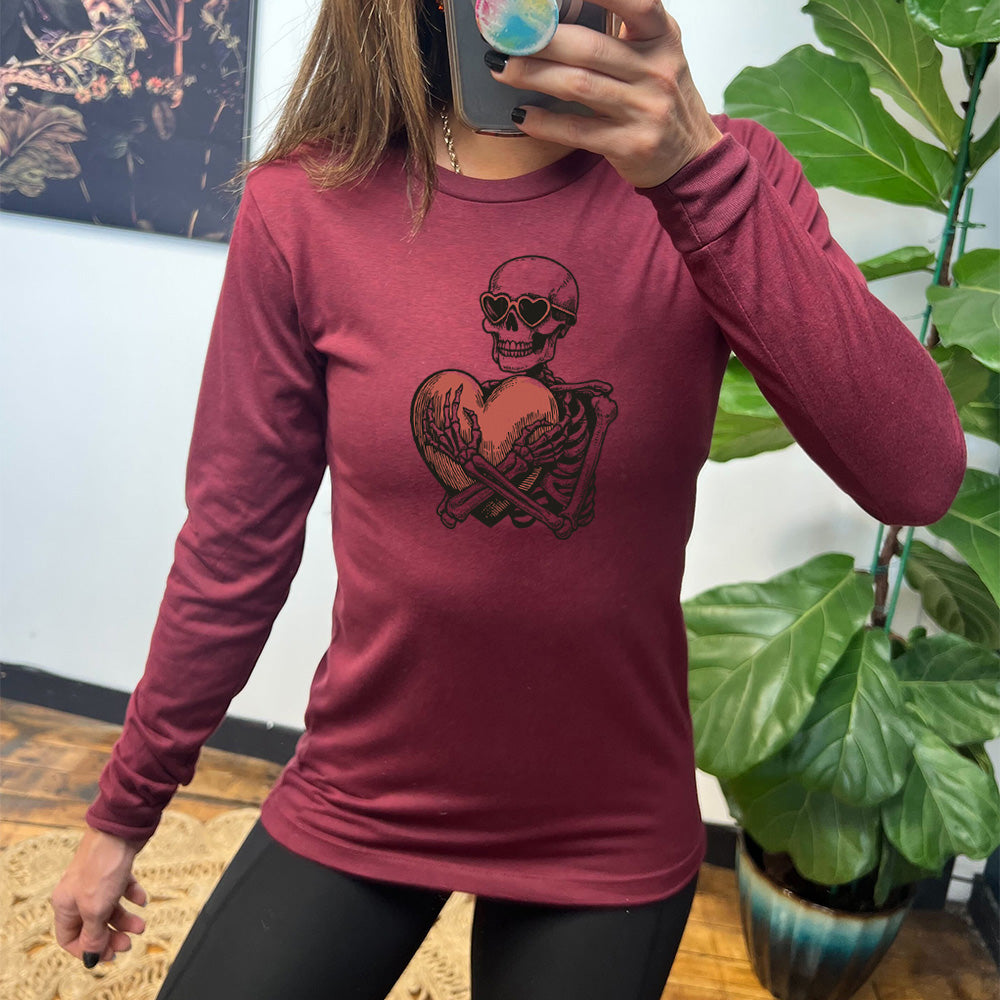 heather cardinal long sleeve shirt with the graphic of a skeleton, wearing sunglasses, hugging a big heart close