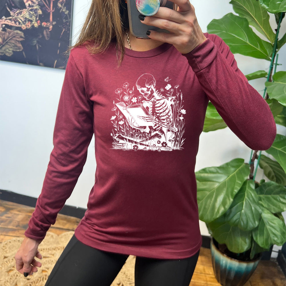 heather cardinal long sleeve shirt with the graphic of a skeleton reading a book, sitting cross-legged in a bed of tall flowers