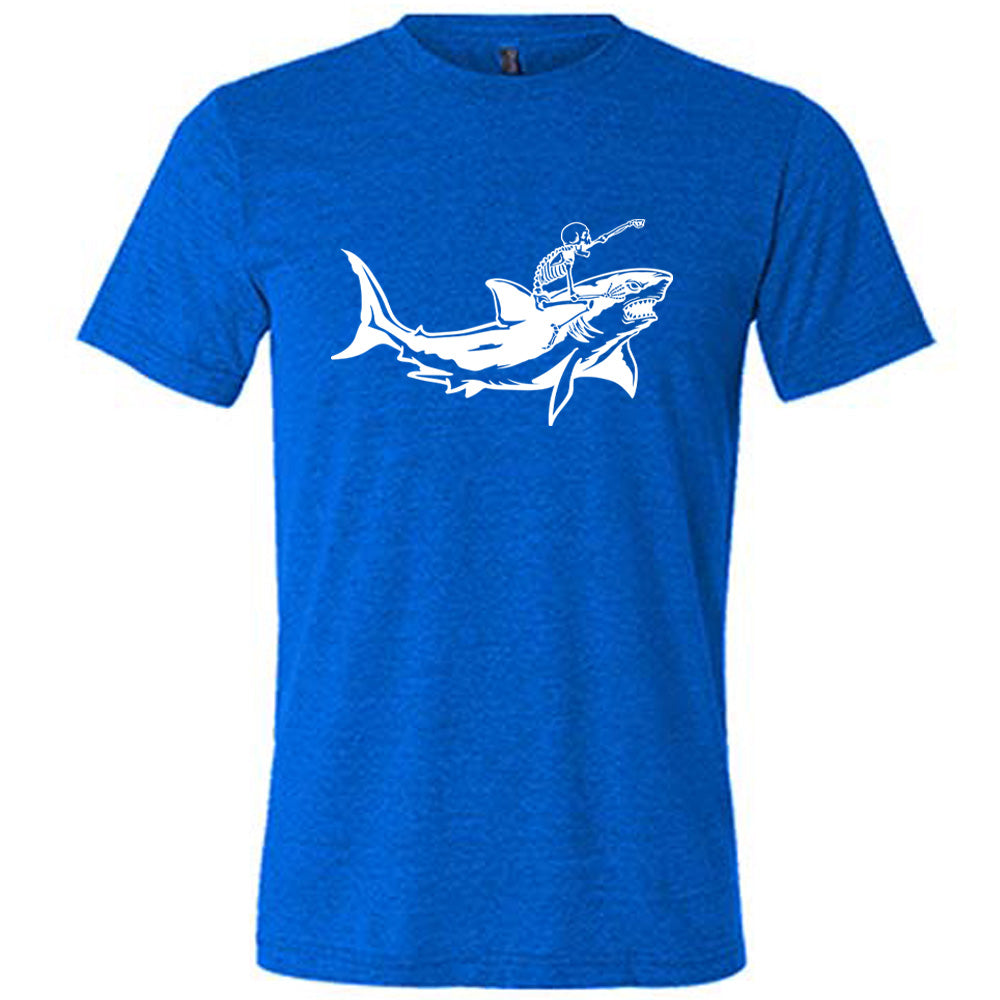 blue unisex tee with the graphic of a skeleton, with its fist pointing onwards and its mouth open, riding a shark, who has a fierce expression