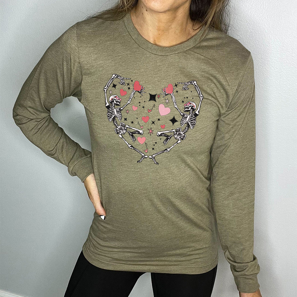 heather olive long sleeve shirt with the graphic of two skeletons creating the shape of a heart with their bodies, appearing to be dancing, with many hearts between them, and a few little stars