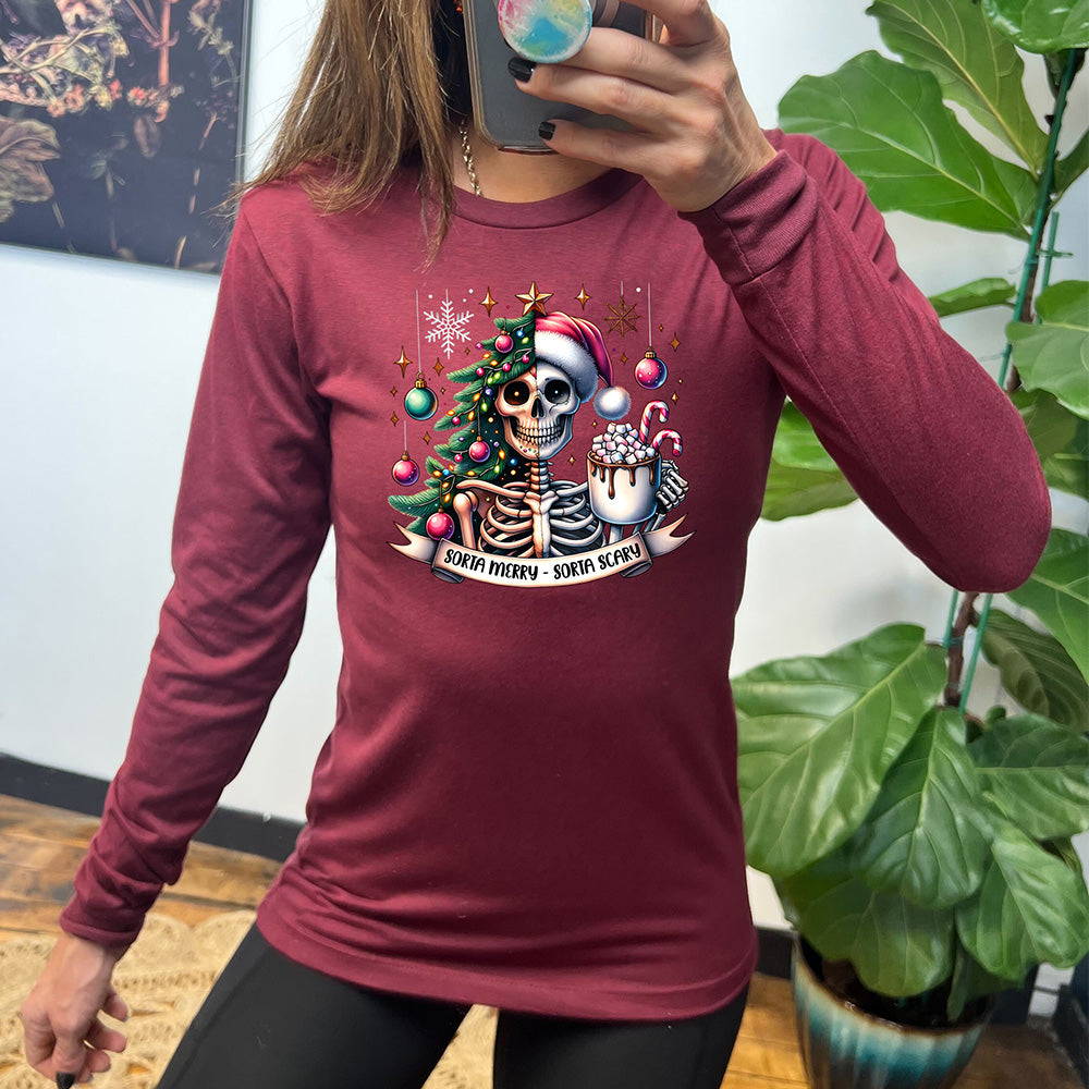 heather cardinal long sleeve shirt with the words "Sorta merry - sorta scary" on it, below the graphic of a skeleton with half its body mixed with a Christmas tree and ornaments and a snowflake, and other half with a Santa hat on, holding a mug piled high with marshmallows and a candy cane ,and some more ornaments