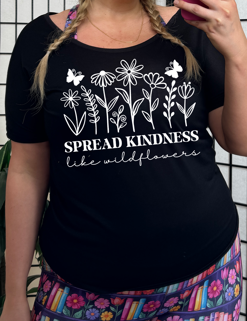 Black slouchy tee with the graphics of wildflowers in a row, with the words "spread kindness like wildflowers" written underneath