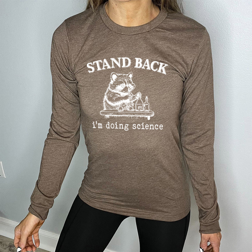 heather brown long sleeve shirt with the words "stand back i'm doing science" on it, with the graphic of a racoon with its paws raised over various bottles