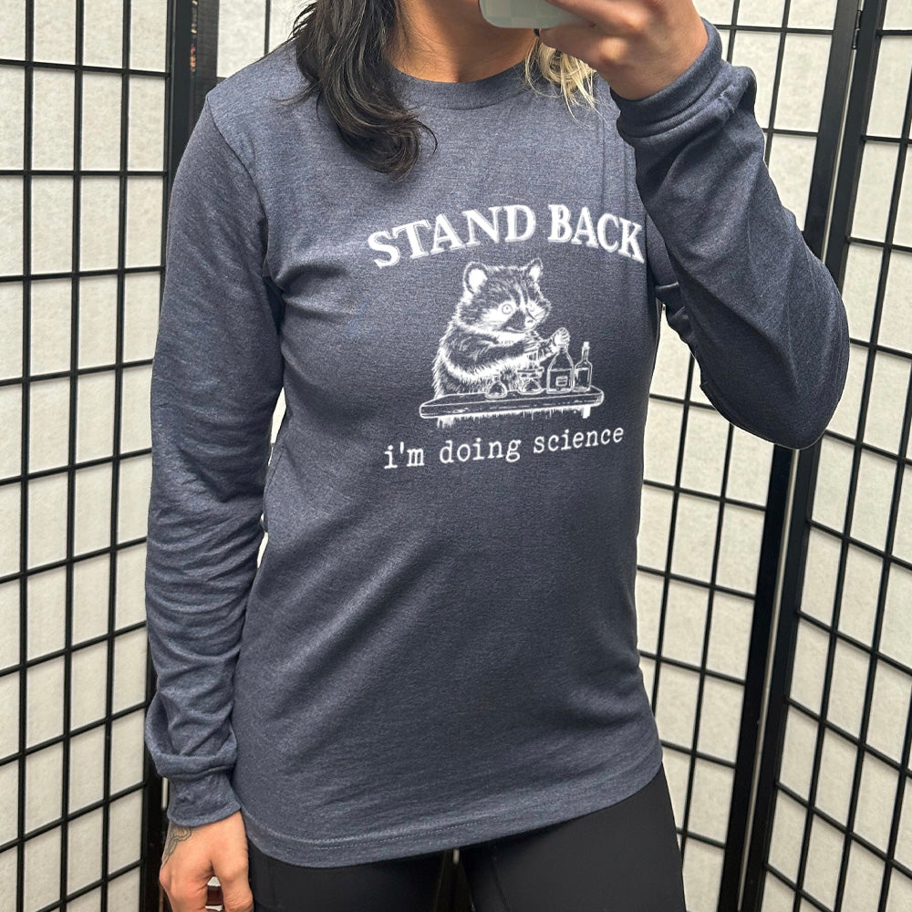 heather navy long sleeve shirt with the words "stand back i'm doing science" on it, with the graphic of a racoon with its paws raised over various bottles