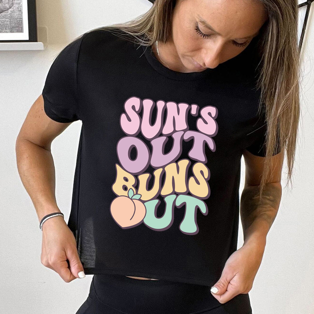 Model wearing black colored cropped tee with a peach graphic on it that says "Suns Out Buns Out"