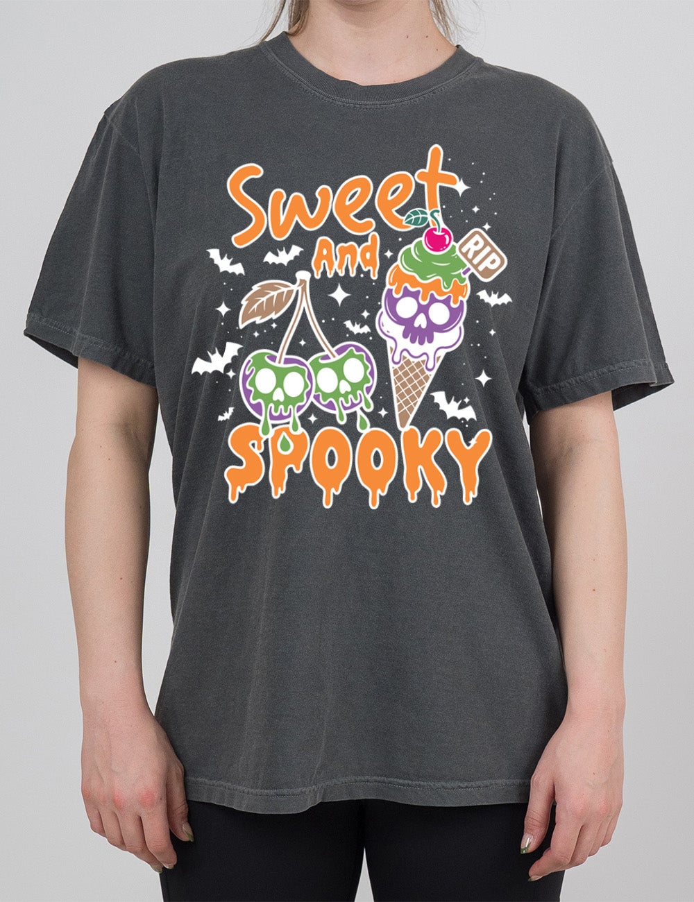 pepper modern tee with the graphic of two cherries on the same branch, with a skull dripping on each of them, and a cherry-topped ice cream cone, with one of the scoops being a skull, with a little "RIP" sign sticking out of the cone, surrounded by bats and stars, and the words starting on top and ending below the graphics saying "sweet and spooky"