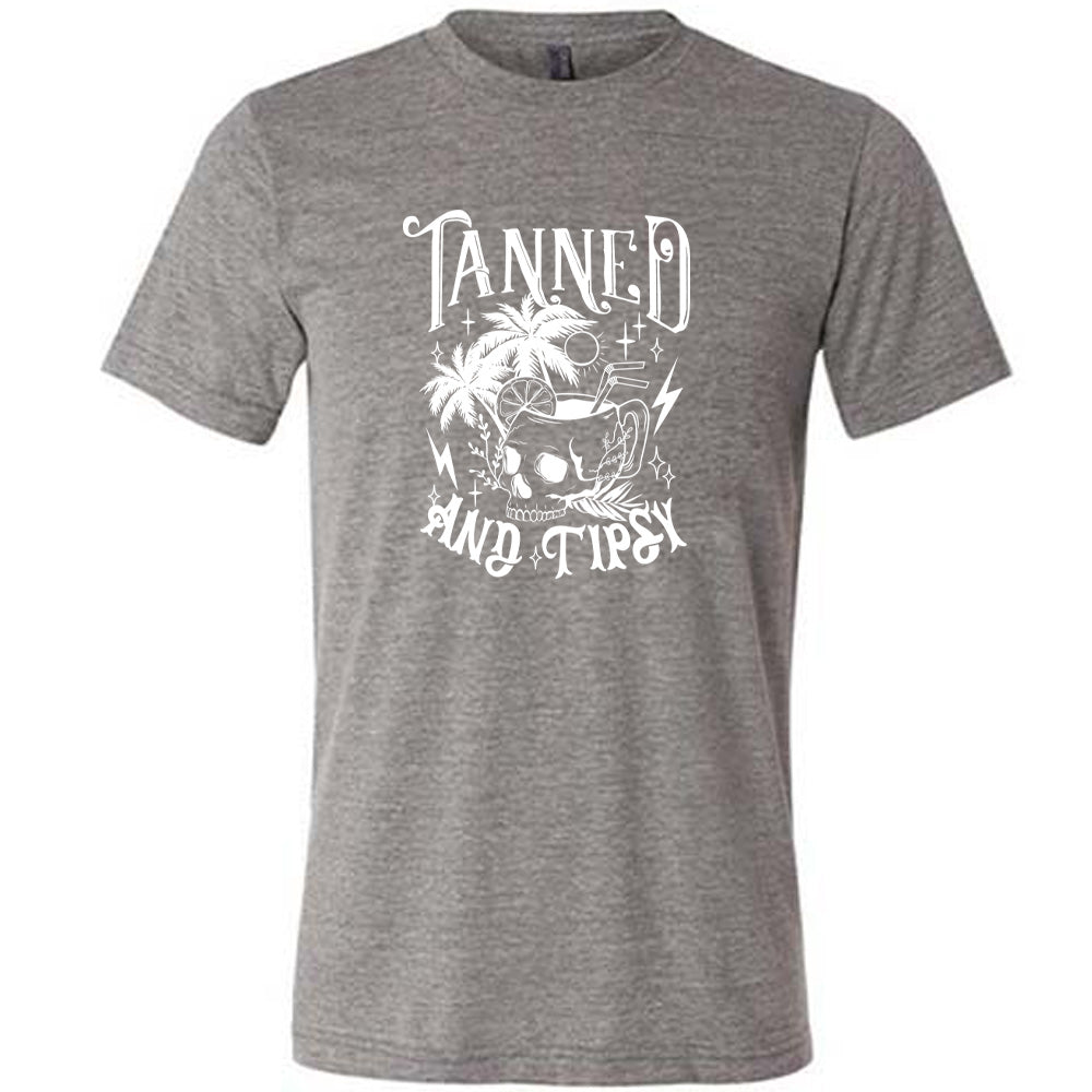 Grey colored shirt with a drink inside a skull cup graphic on it that says "Tanned and Tipsy"