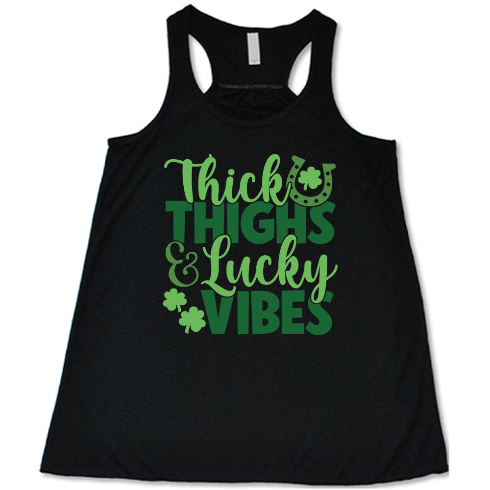 black flowy tank with the words "thick thighs & lucky vibes" on it, with graphics of a horseshoe and a few shamrocks