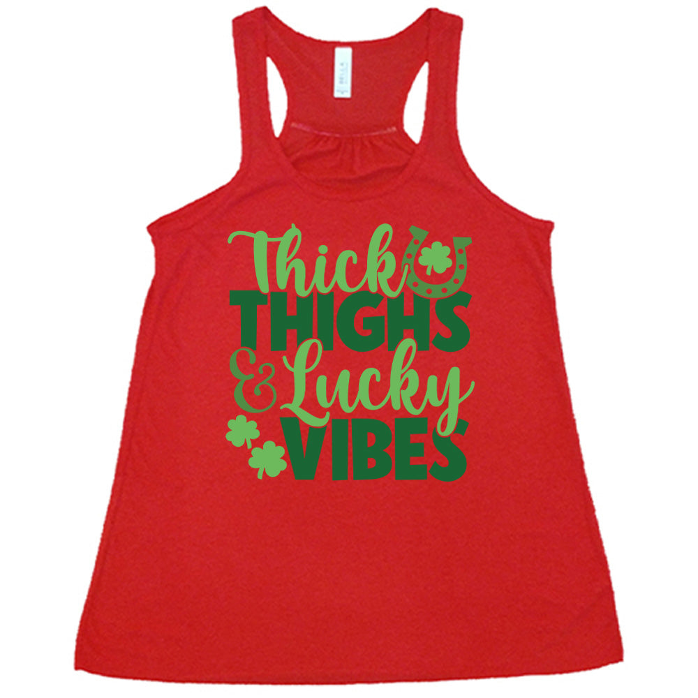red flowy tank with the words "thick thighs & lucky vibes" on it, with graphics of a horseshoe and a few shamrocks