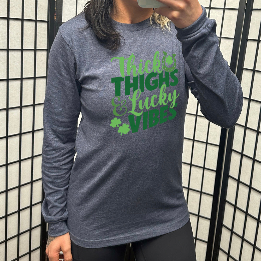 heather navy long sleeve with the words "thick thighs & lucky vibes" on it, with graphics of a horseshoe and a few shamrocks