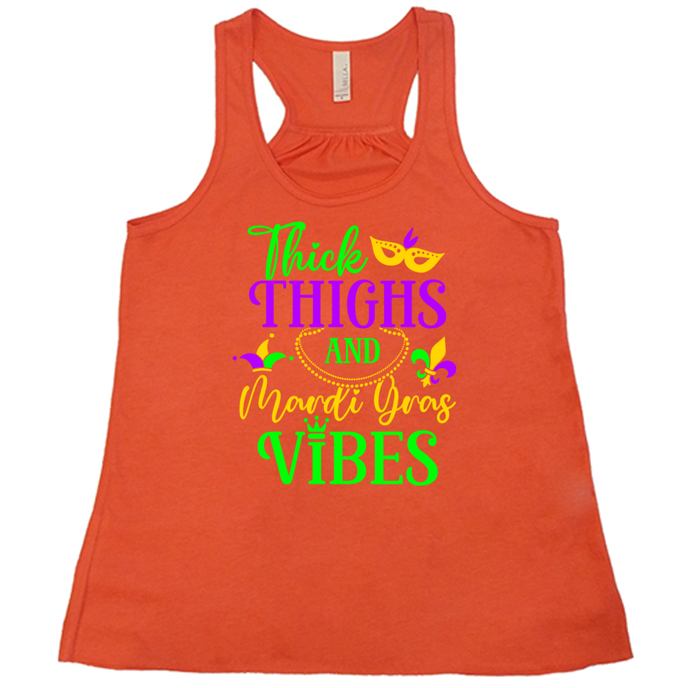 coral flowy tank with the words "thick thighs and mardi gras vibes" on it in varying font, with small graphics of mardi gras beads, fleur de lis, a joker hat and a mask
