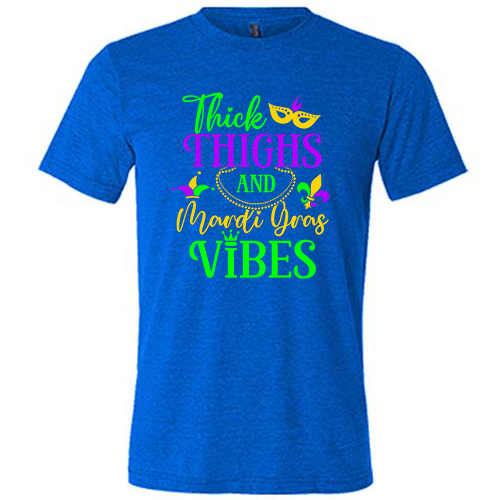 blue unisex tee with the words "thick thighs and mardi gras vibes" on it in varying font, with small graphics of mardi gras beads, fleur de lis, a joker hat and a mask