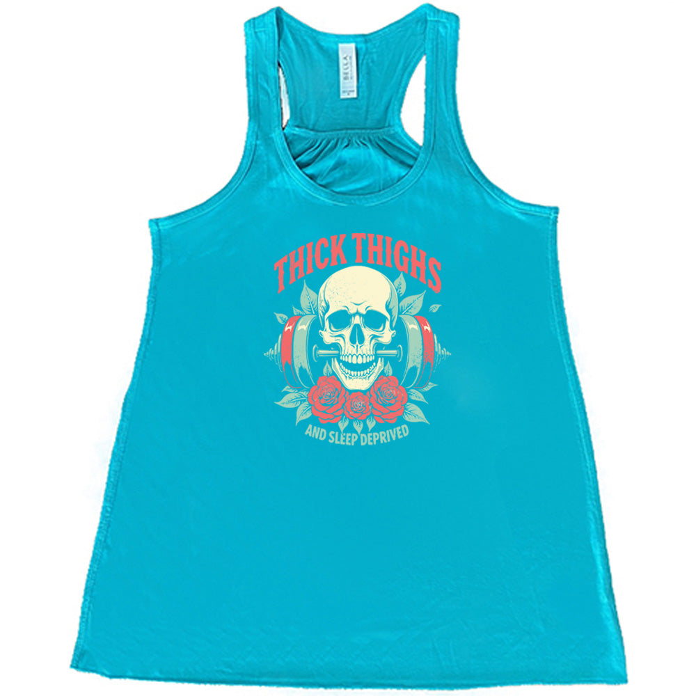 Teal colored flowy tank with a skull, flowers, and barbell graphic on it that says "Thick Thighs And Sleep Deprived"