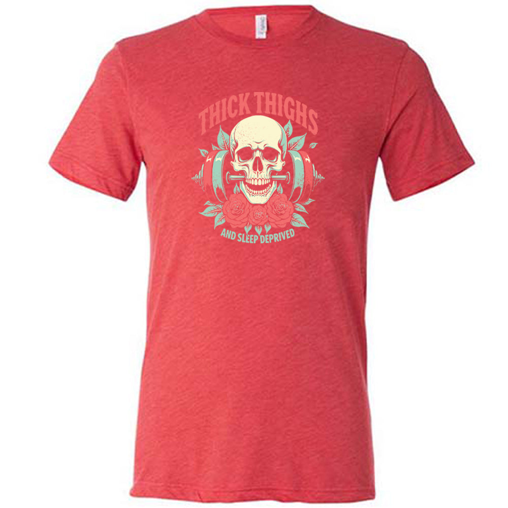 Red colored shirt with a skull, flowers, and barbell graphic on it that says "Thick Thighs And Sleep Deprived"