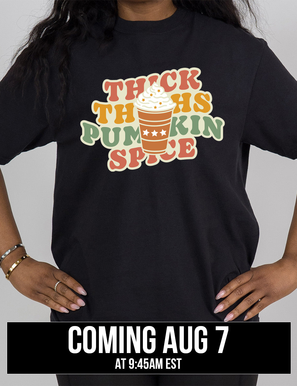 black modern tee with the words "thick thighs pumpkin spice" on it, with the graphic of a pumpkin spice latte, topped with whipped cream, in front of the words coming august 7th