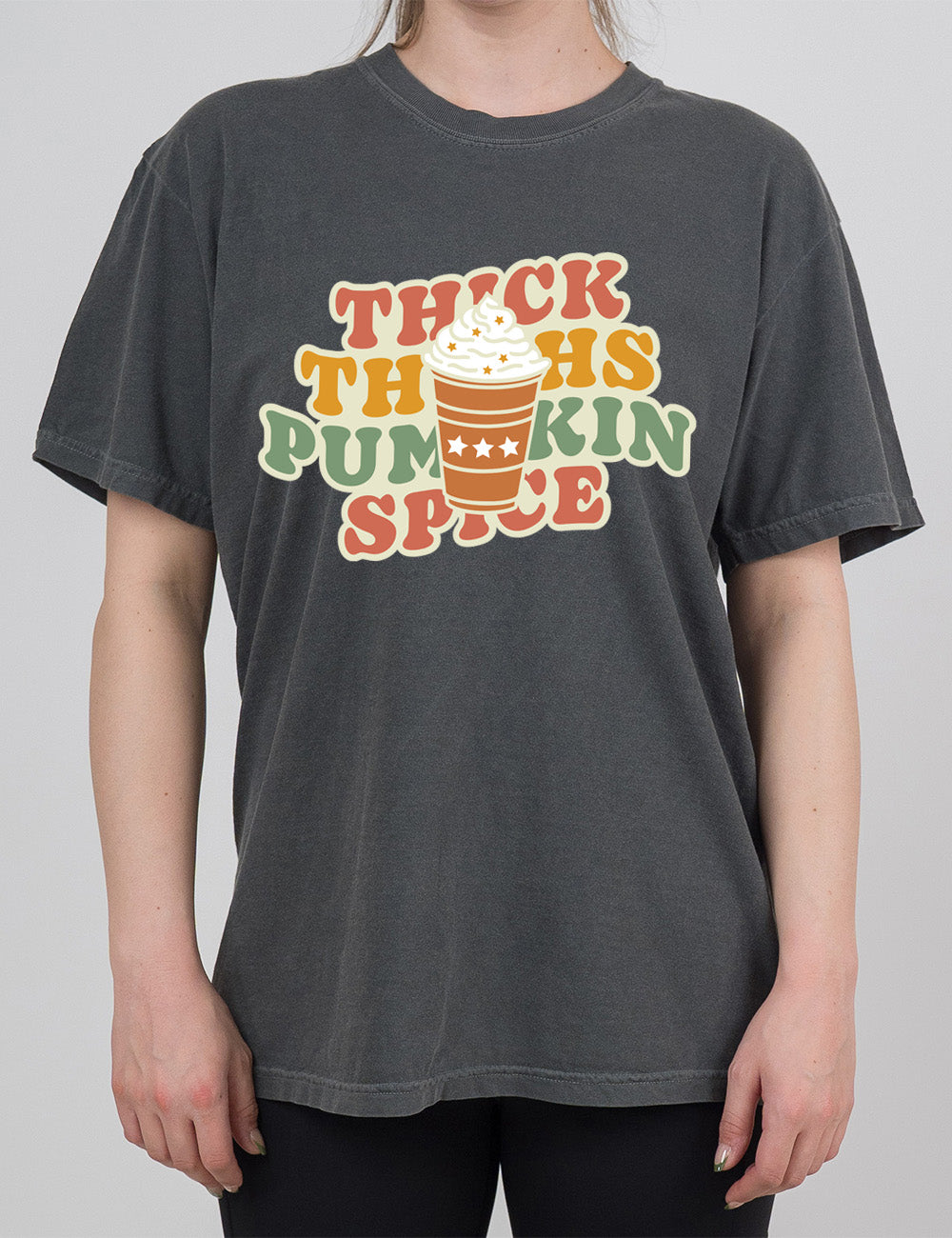 pepper modern tee with the words "thick thighs pumpkin spice" on it, with the graphic of a pumpkin spice latte, topped with whipped cream, in front of the words