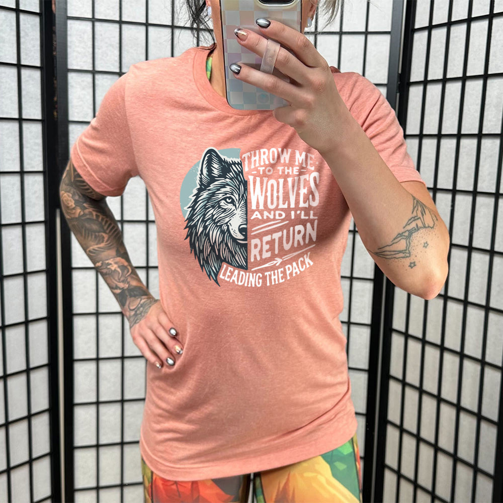 Model wearing sunset colored shirt with a wolf face graphic on it that says "Throw Me To The Wolves And I'll Return Leading the Pack"