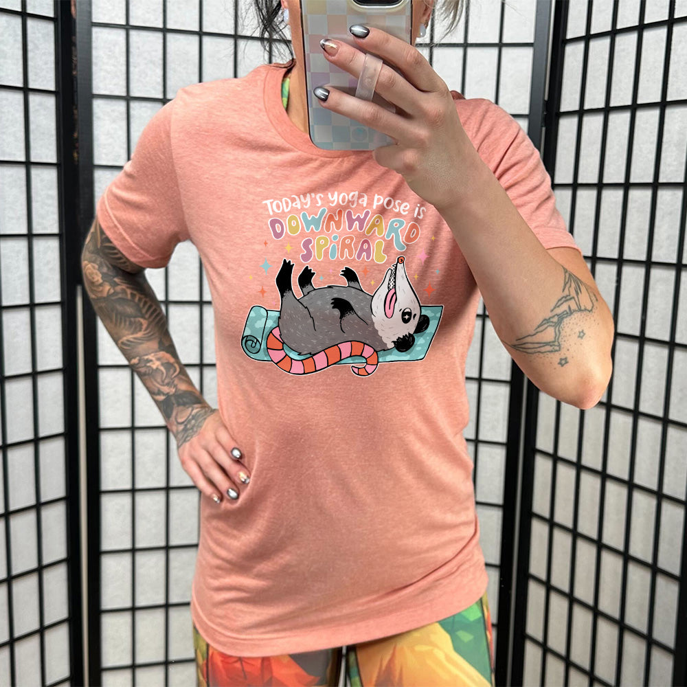 Sunset unisex tee with the words "Today's yoga pose is a downward spiral" and the graphic of a possum playing dead on a yoga mat