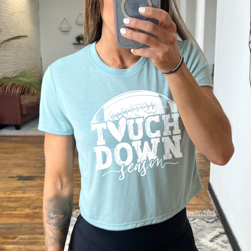 Model wearing dusty blue colored cropped tee with football graphic on it that says "Touchdown Season"
