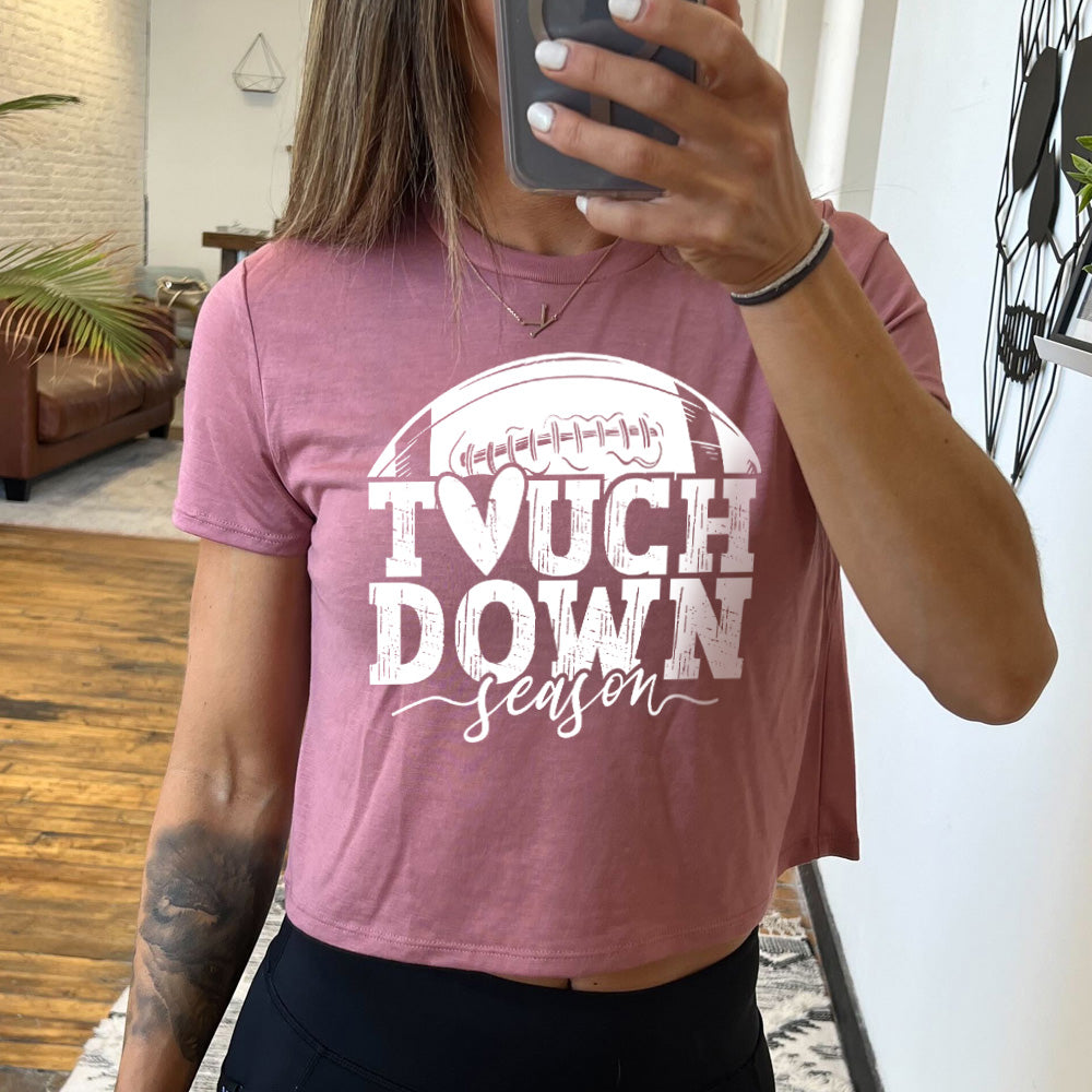 Model wearing mauve colored cropped tee with football graphic on it that says "Touchdown Season"