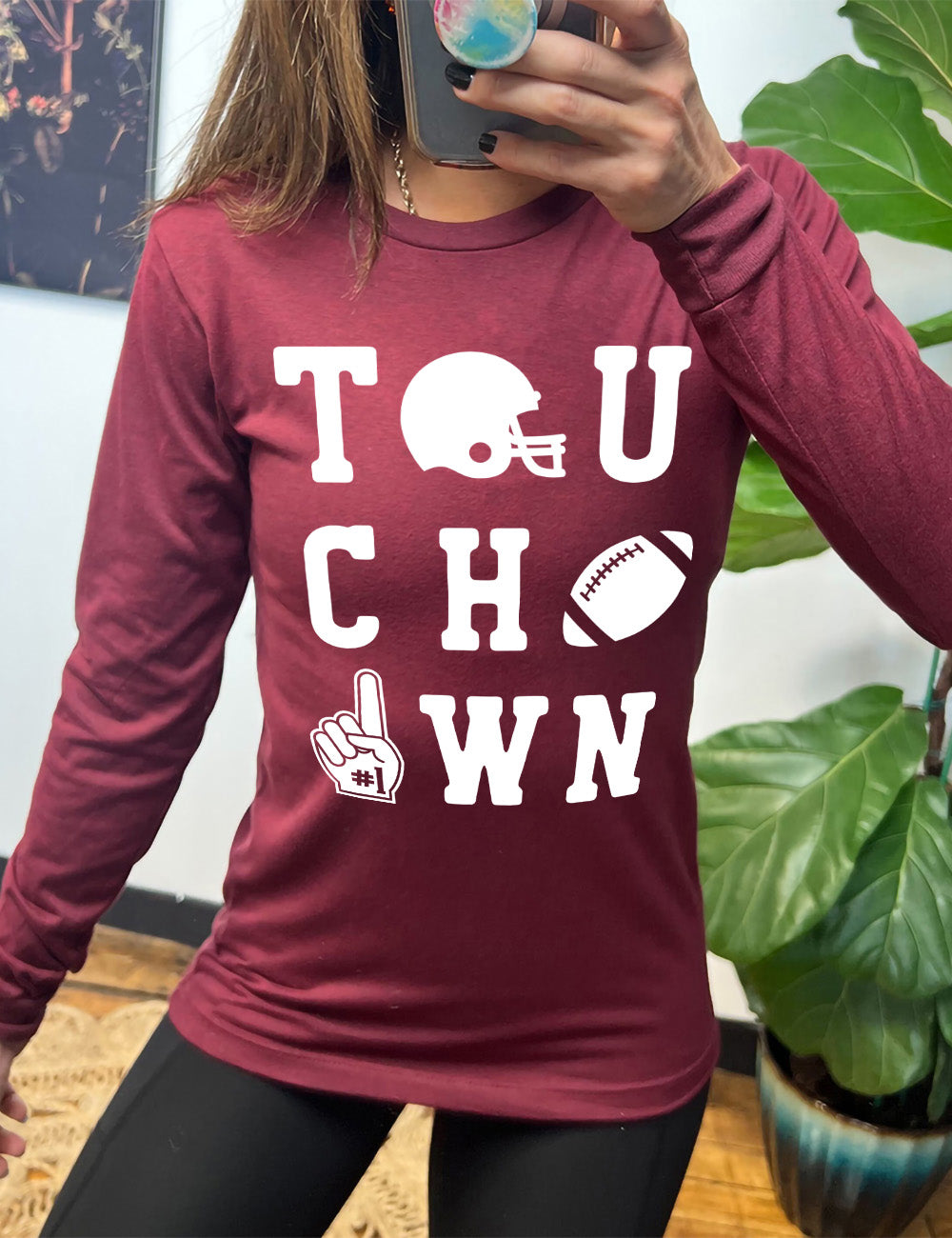 heather cardinal long sleeve tee with the word "touchdown" spelled out over three rows, and with the first "o" being a football helmet, the "d" being a football, and the last "o" being a foam finger with #1 on it
