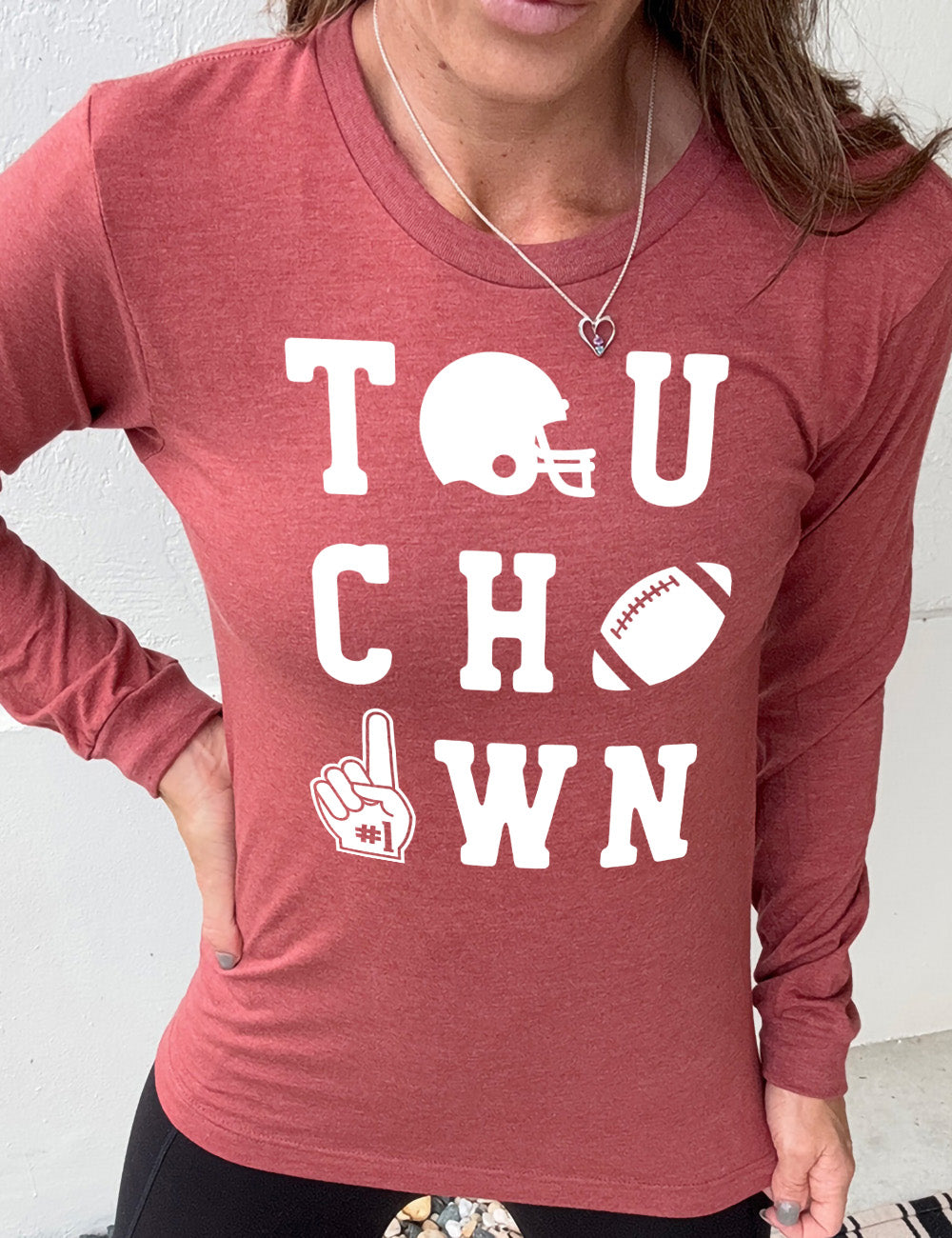 heather clay long sleeve tee with the word "touchdown" spelled out over three rows, and with the first "o" being a football helmet, the "d" being a football, and the last "o" being a foam finger with #1 on it