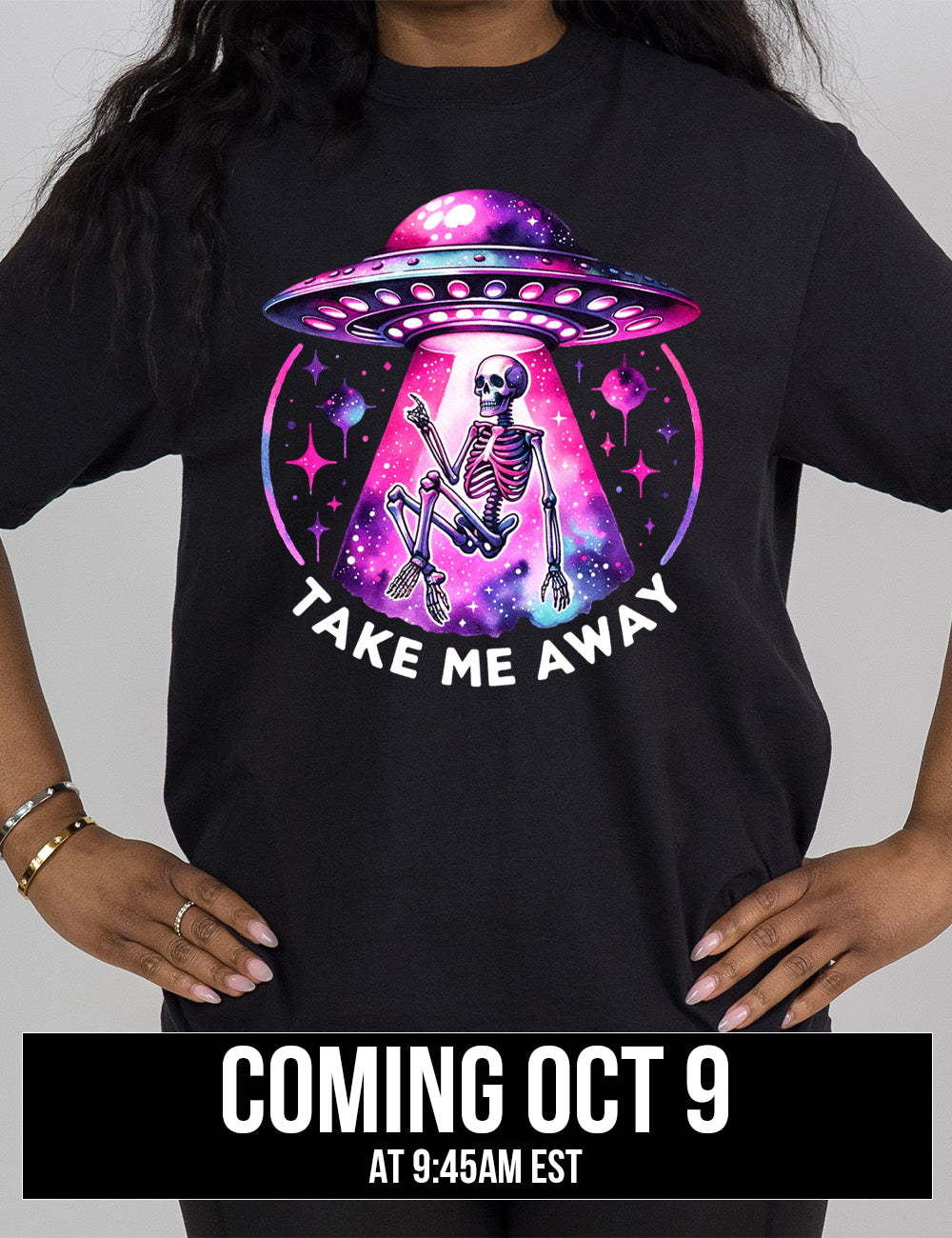 black modern tee with the colorful and detailed graphic of an alien spaceship, above little planets and stars, beaming up a skeleton, and the words underneath saying "take me away" Coming October 9th