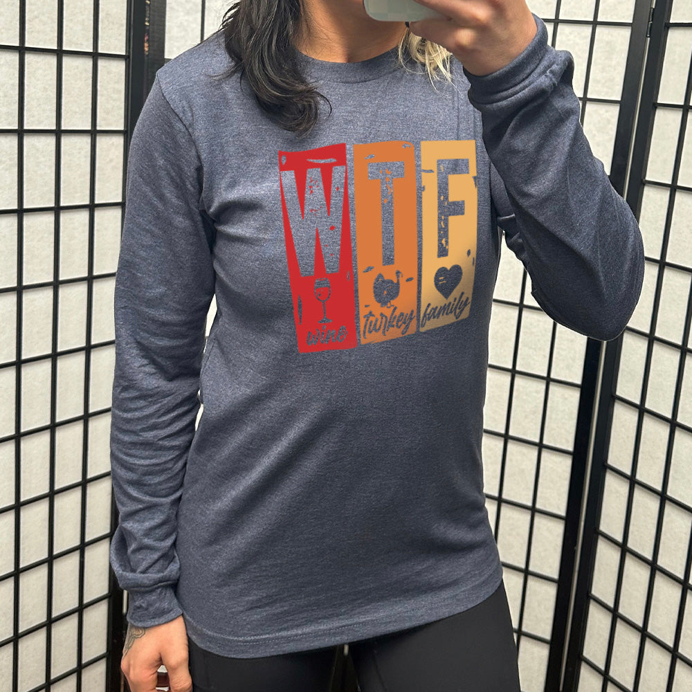 heather navy long sleeve shirt with a graphic on it that says "WTF" and under the "W" there's a graphic of a wine glass and the word "wine"; under "T" there's a graphic of a turkey and the word "turkey"; under F there's a graphic of a heart and the word "family"