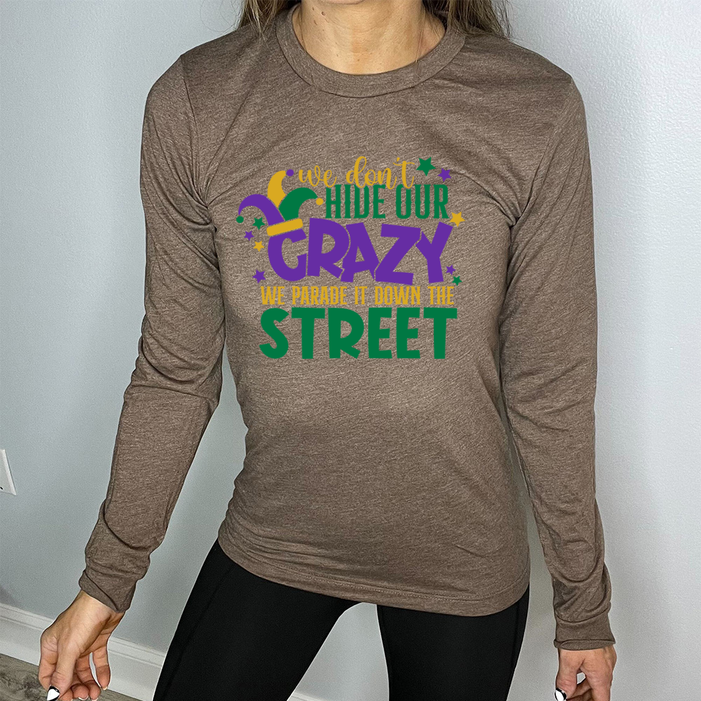 heather brown long sleeve tee with the words "we don't hide our crazy we parade it down the street" on it with a joker hat on the letter "c" and a few little stars scattered around