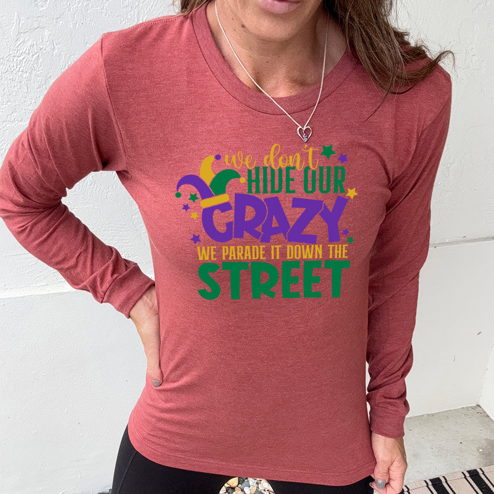 heather clay long sleeve tee with the words "we don't hide our crazy we parade it down the street" on it with a joker hat on the letter "c" and a few little stars scattered around