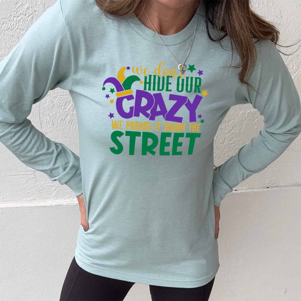 heather dusty blue long sleeve tee with the words "we don't hide our crazy we parade it down the street" on it with a joker hat on the letter "c" and a few little stars scattered around