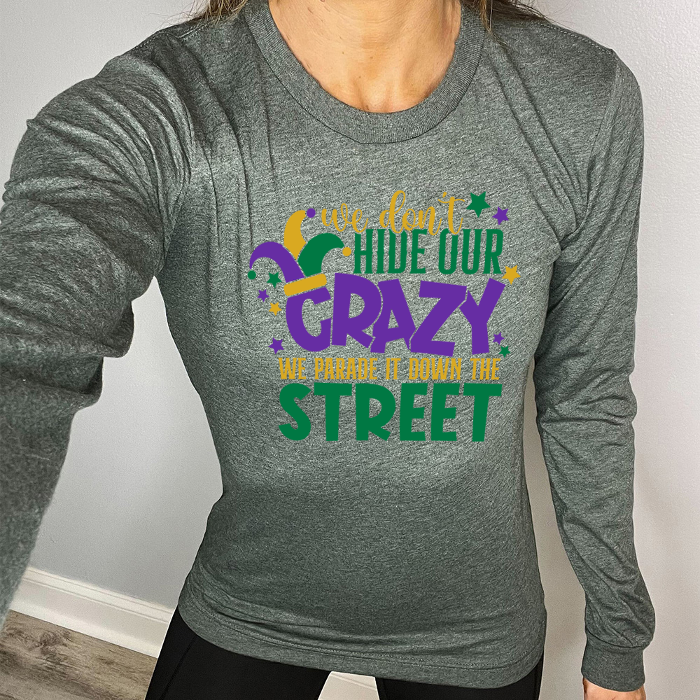 heather forest long sleeve tee with the words "we don't hide our crazy we parade it down the street" on it with a joker hat on the letter "c" and a few little stars scattered around