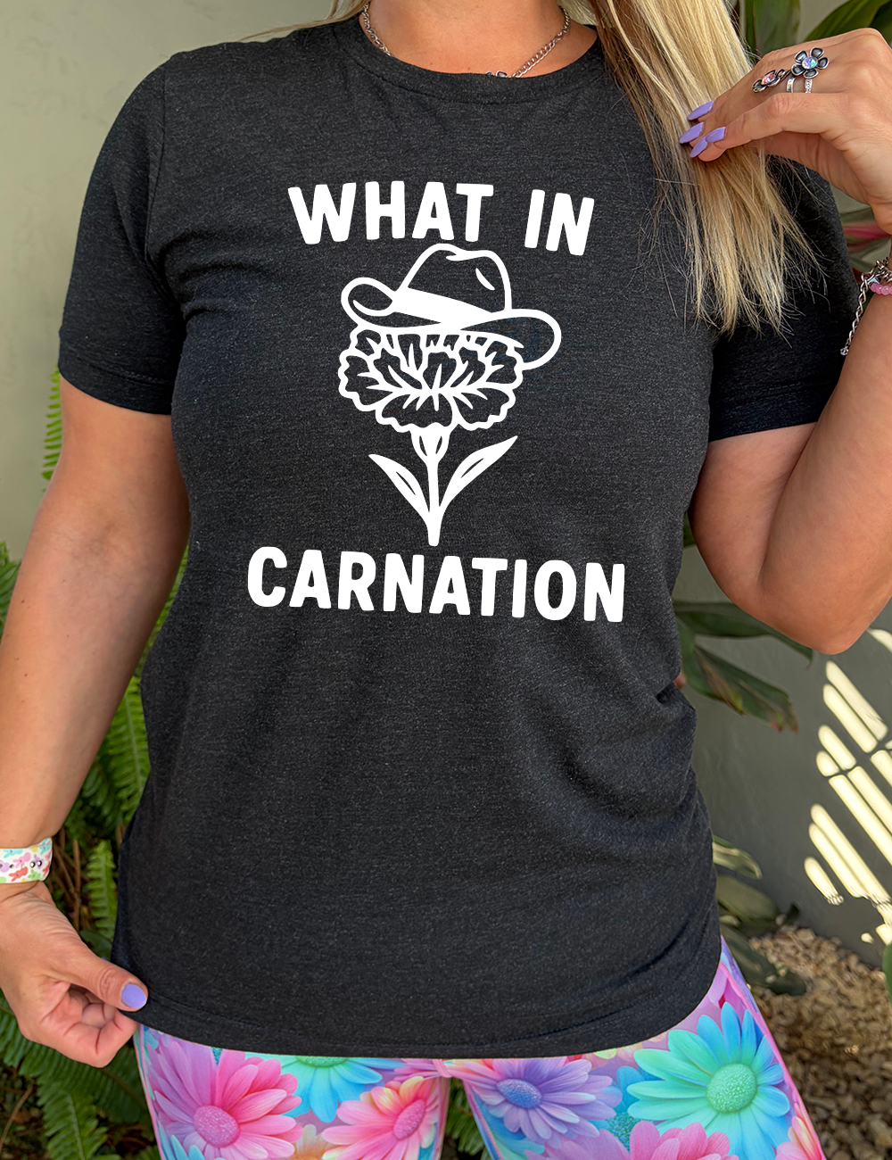 black unisex tee with the words "What in carnation" on it, around the graphic of a carnation, wearing a cowboy hat