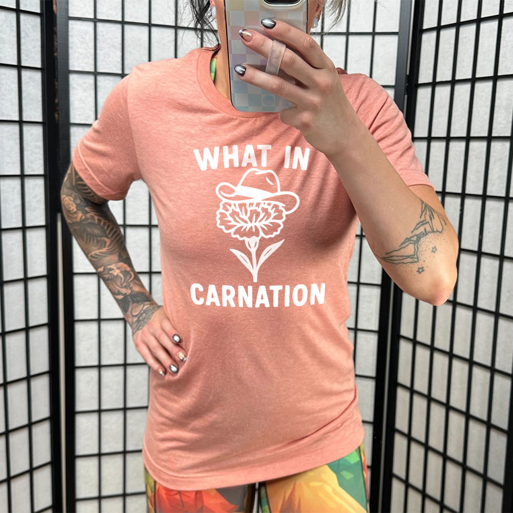 sunset unisex tee with the words "What in carnation" on it, around the graphic of a carnation, wearing a cowboy hat