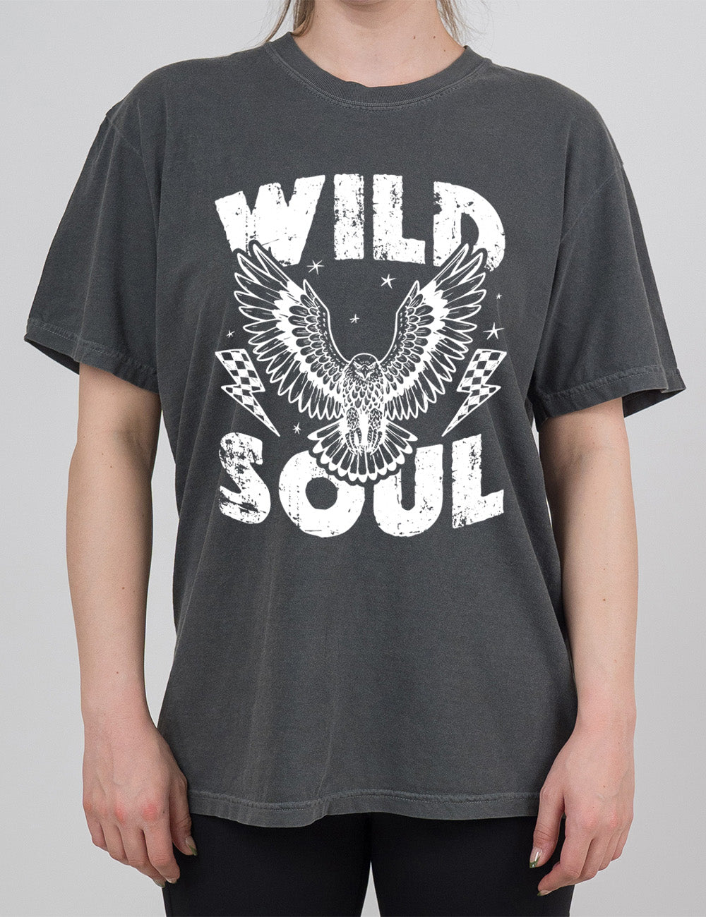 pepper modern tee with print placement on the front, with the words "wild soul" on it, with a large eagle graphic, with wings in flight, in the middle of the words, with a checkered lightning bolt on either side of it, with a few stars scattered around it
