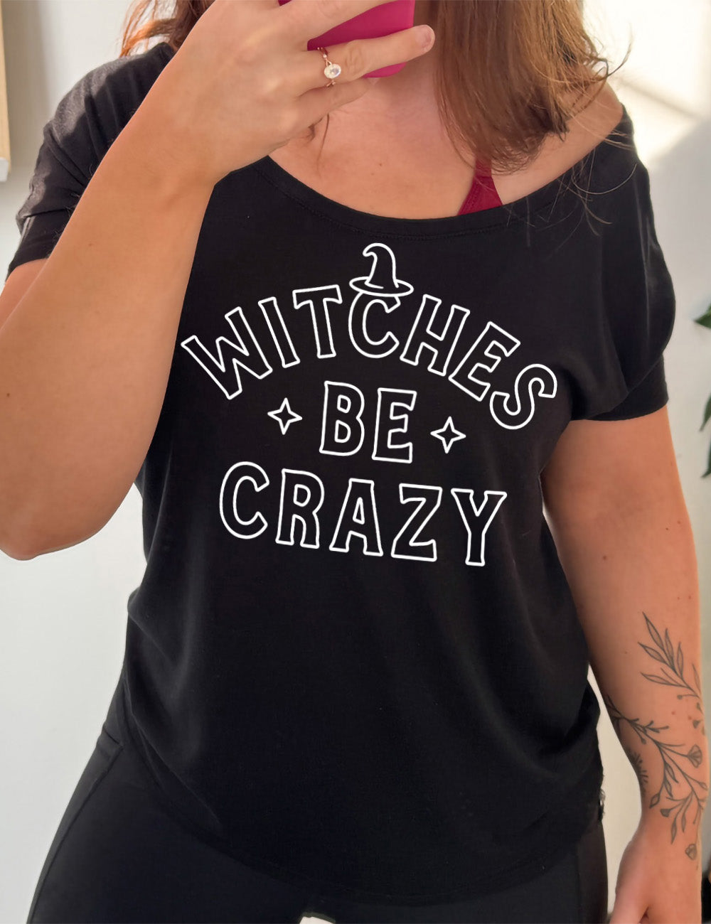 black slouchy tee with the words in outline font saying "witches be crazy" with a witch hat on top of the "c" in "witches" and a star on either side of the word "be"