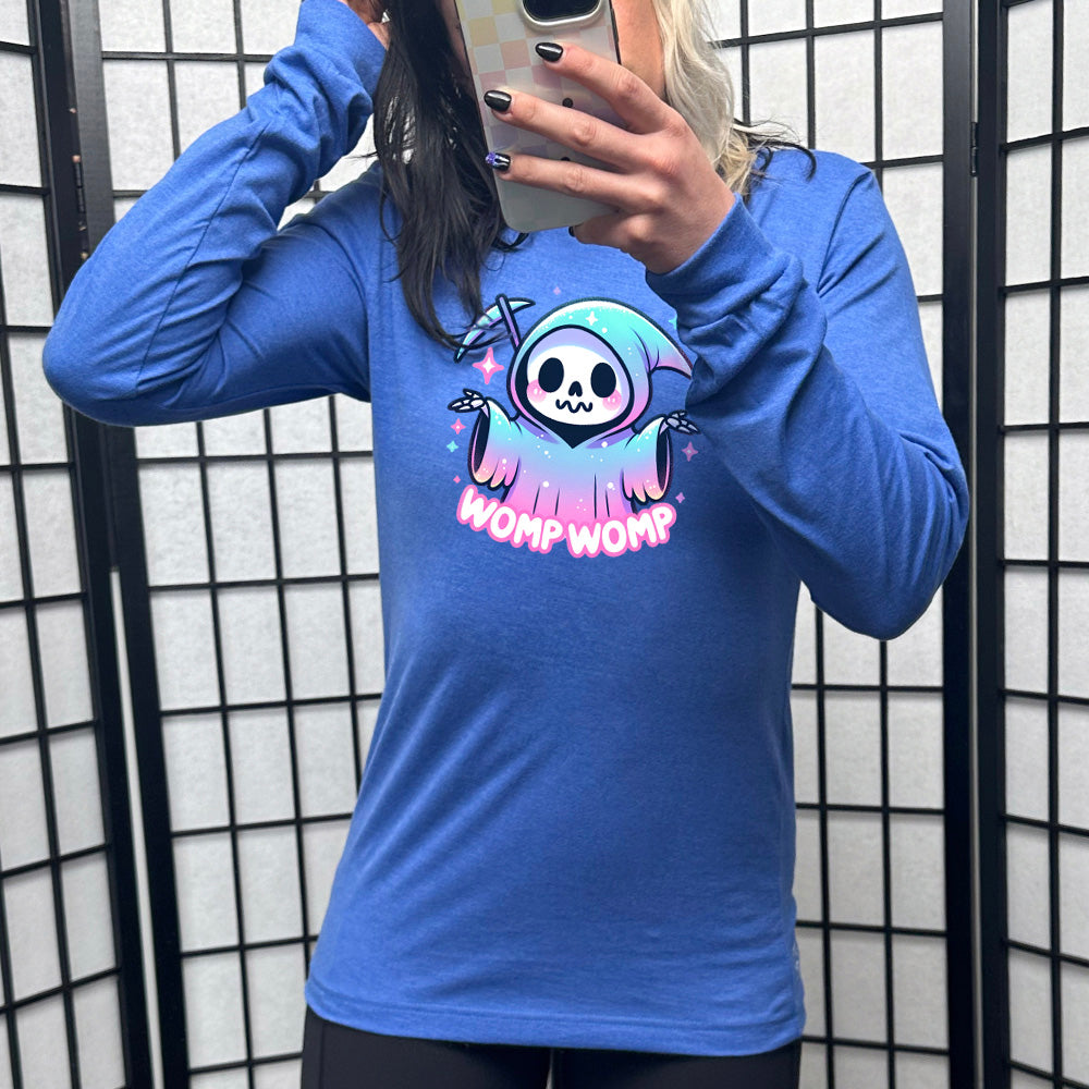 heather true royal long sleeve shirt with the text "Womp Womp" on it, with the cartoon graphic of a sparkly-robed grim reaper, skeletal hands raised in question, surrounded by sparkly little stars