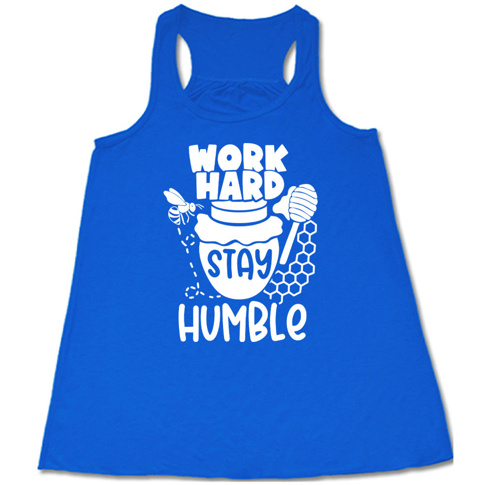 blue flowy racerback tank with the words "work hard stay humble" on it, with the word "stay" on the graphic of a honeypot, and a bee flying around the pot's left, and some honeycomb and a honey spoon on its right