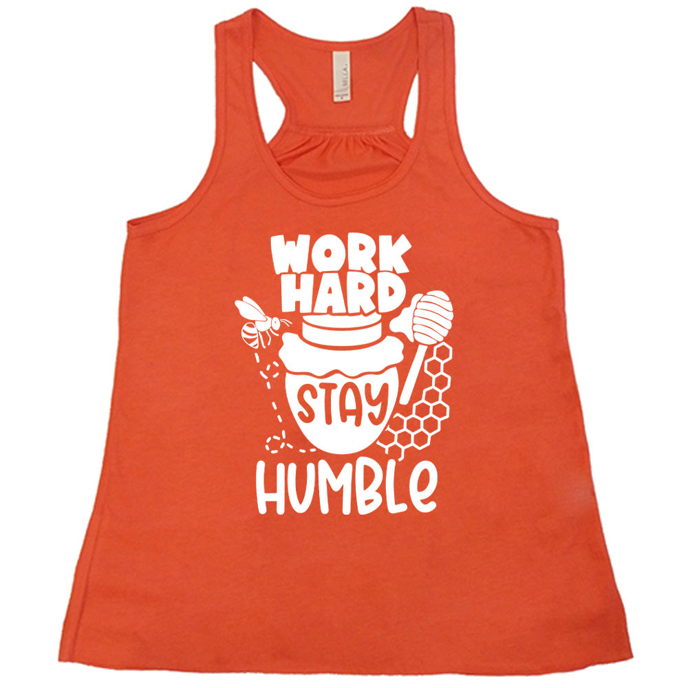 coral flowy racerback tank with the words "work hard stay humble" on it, with the word "stay" on the graphic of a honeypot, and a bee flying around the pot's left, and some honeycomb and a honey spoon on its right