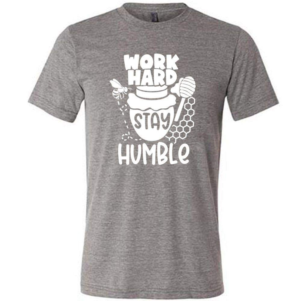 grey unisex tee with the words "work hard stay humble" on it, with the word "stay" on the graphic of a honeypot, and a bee flying around the pot's left, and some honeycomb and a honey spoon on its right