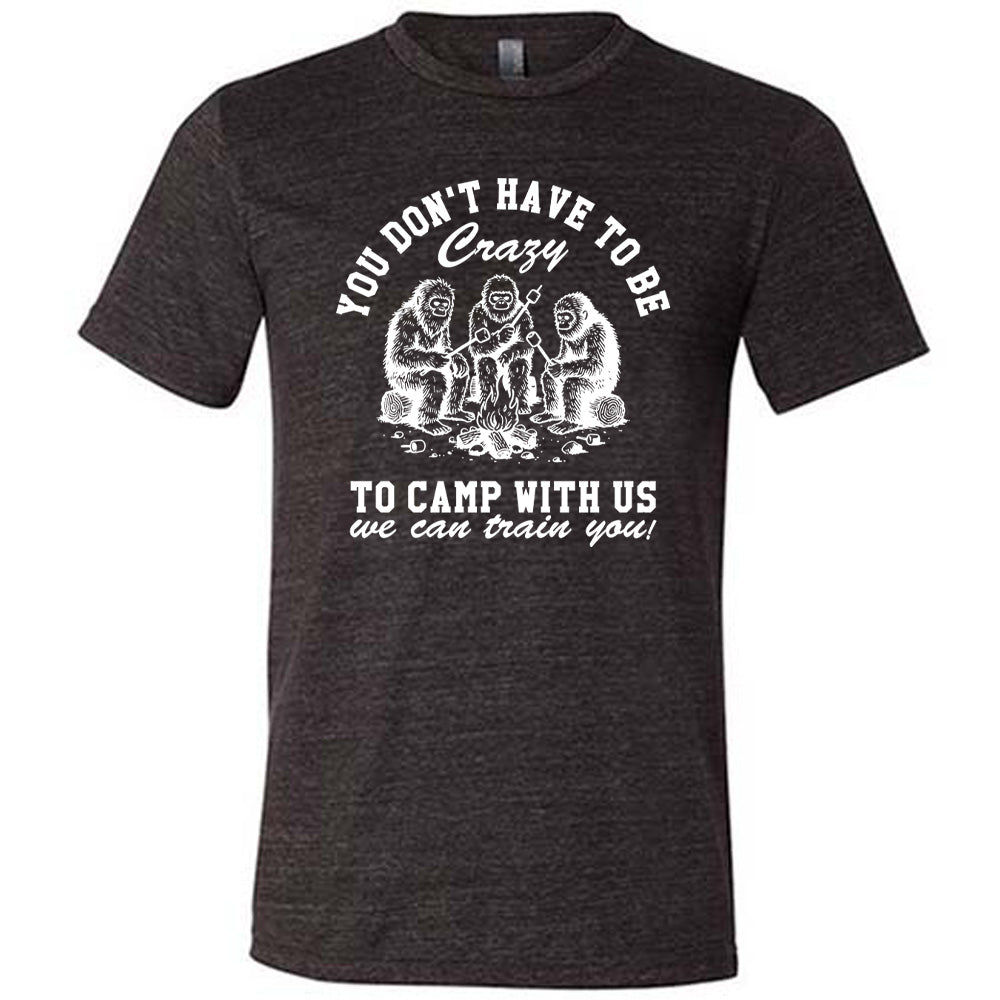 black unisex tee with the words "you don't have to be crazy to camp with us we can train you!" on it with the graphic of three sasquatches toasting marshmallows over a campfire