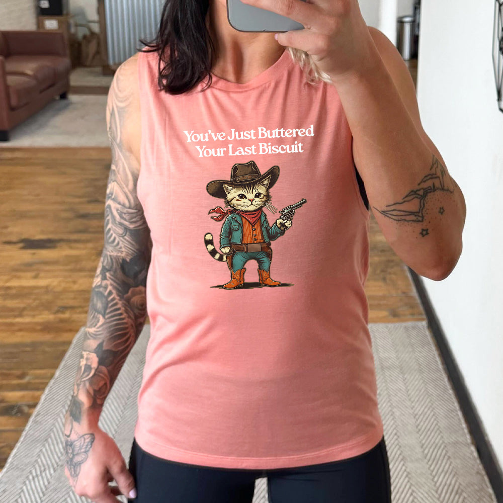 peach muscle tank with a cat wearing cowboy gear graphic on it that says "You've Just Buttered Your Last Biscuit"