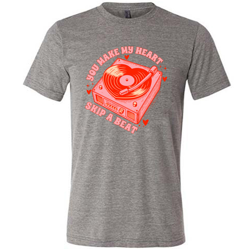 grey unisex tee with the words "you make my heart skip a beat" on it, with the graphics of a record player, with a record shaped like a heart, with a little hearts and stars around each corner of the player