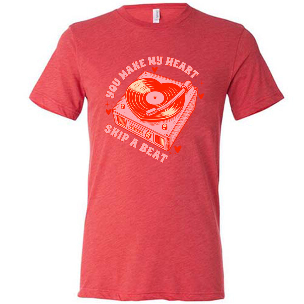 red unisex tee with the words "you make my heart skip a beat" on it, with the graphics of a record player, with a record shaped like a heart, with a little hearts and stars around each corner of the player
