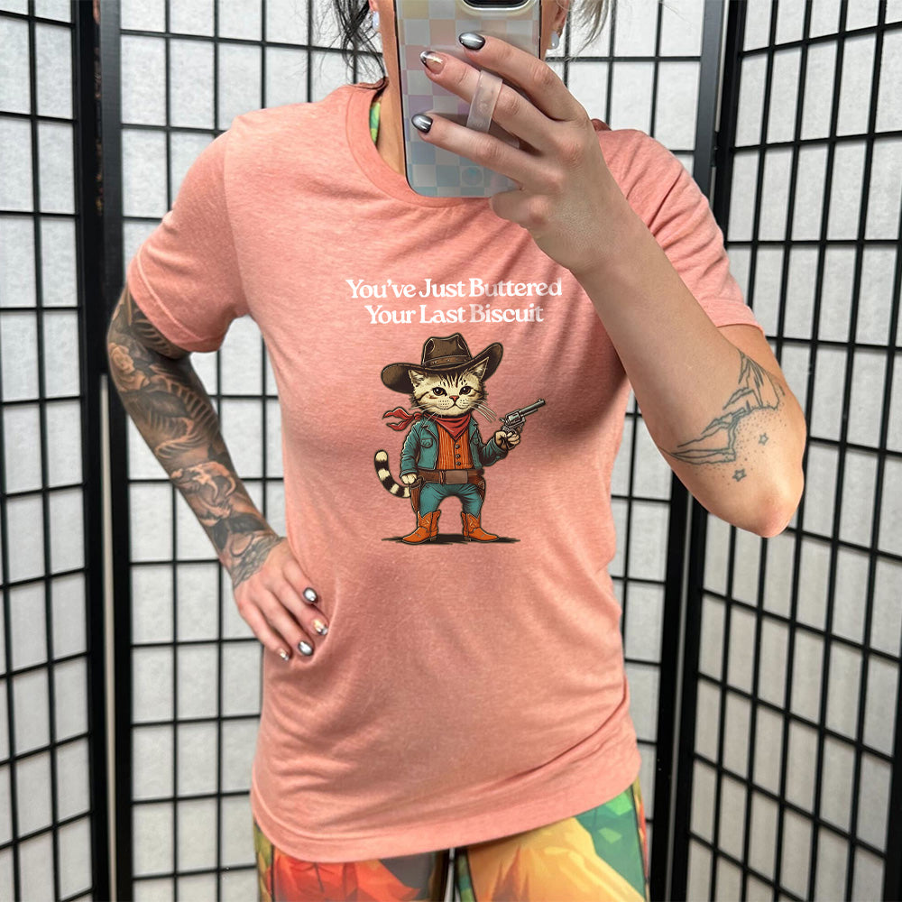 Sunset colored shirt with a cowboy cat graphic on it that says "You've Just Buttered Your Last Biscuit"