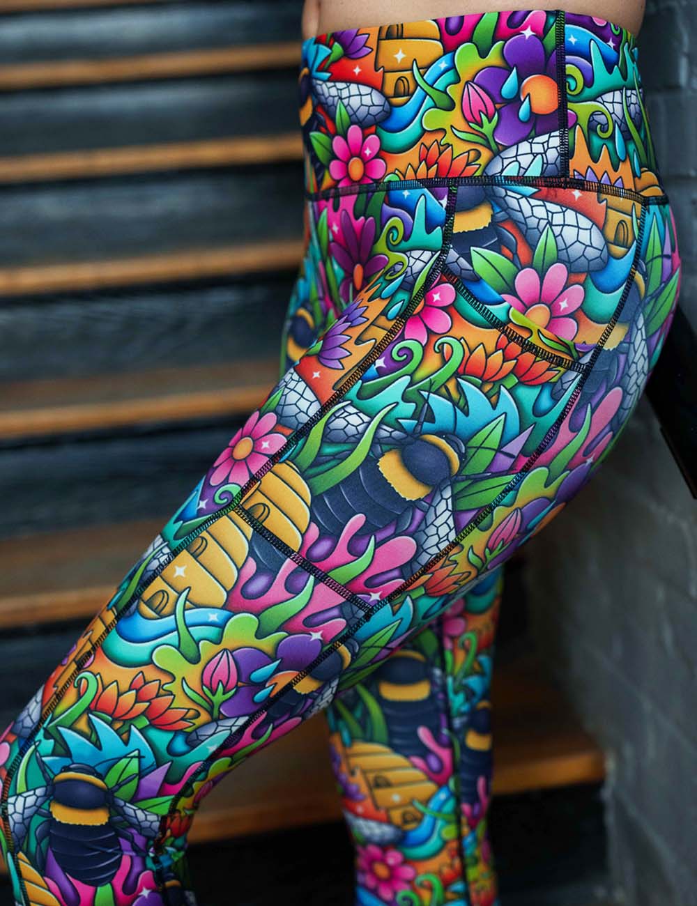 cartoon bees against bold colorful cartoon flowers pattern leggings close up against a white background