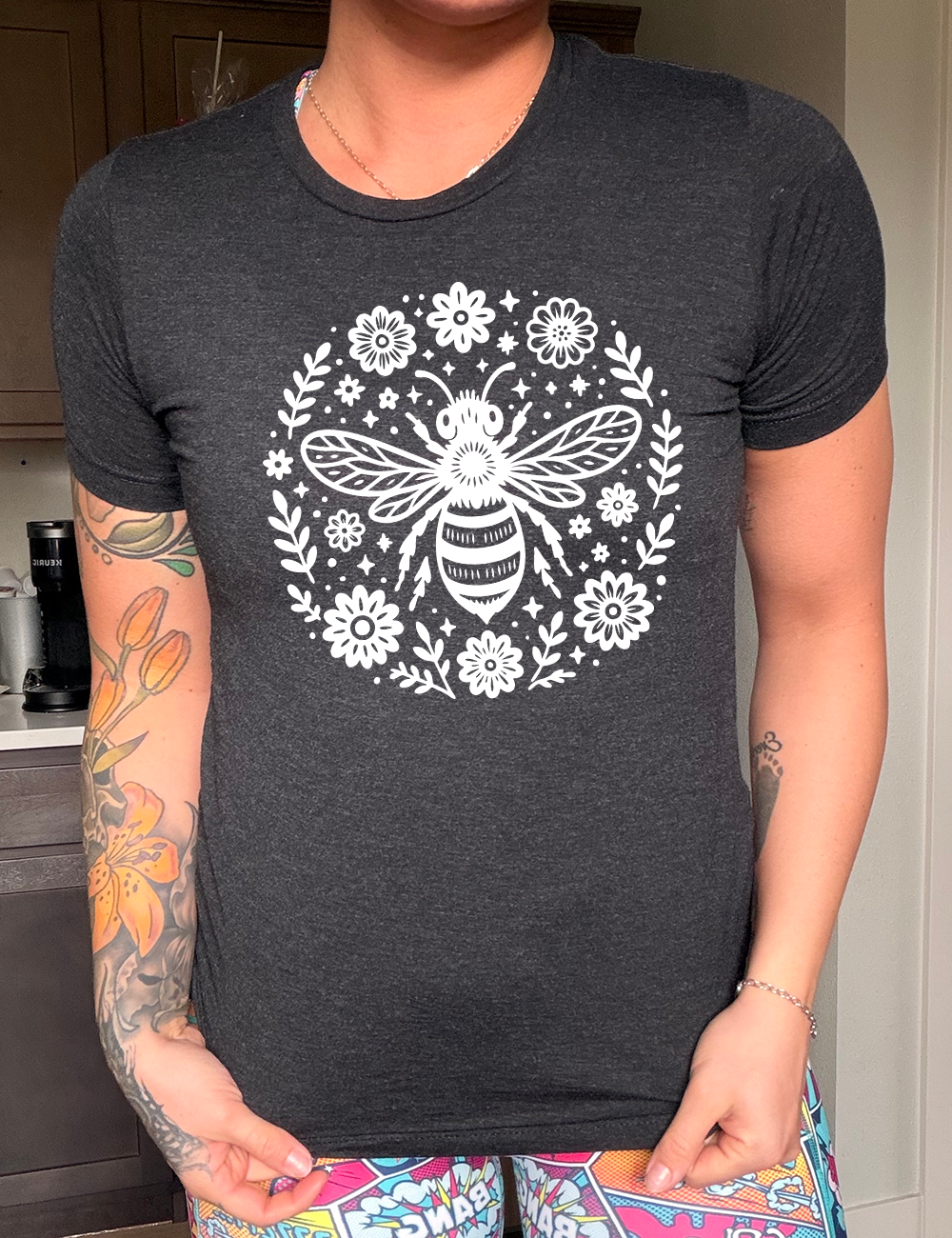 black unisex tee with the graphic of a boho circled design filled with flowers of varied size, some branches, some stars, and in the center a fancy bee